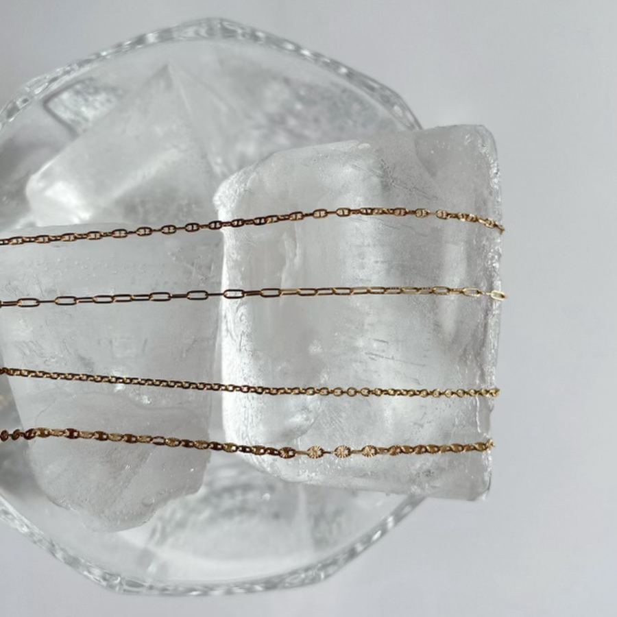 Golden permanent jewelry chains laid over a crystal bowl. Vixen Collection Boutique Seattle, WA