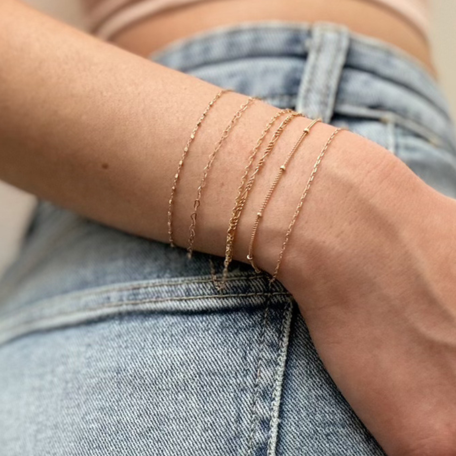 A woman's wrist wearing permanent jewelry. Fingers tucked into her jean's front pocket. Permanent Jewelry services now available at Vixen Collection Boutique in Seattle, WA.