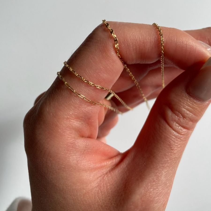 Woman's hand and fingers holding 4 different gold permanent jewelry chain options. Vixen Collection Boutique Seattle, WA.