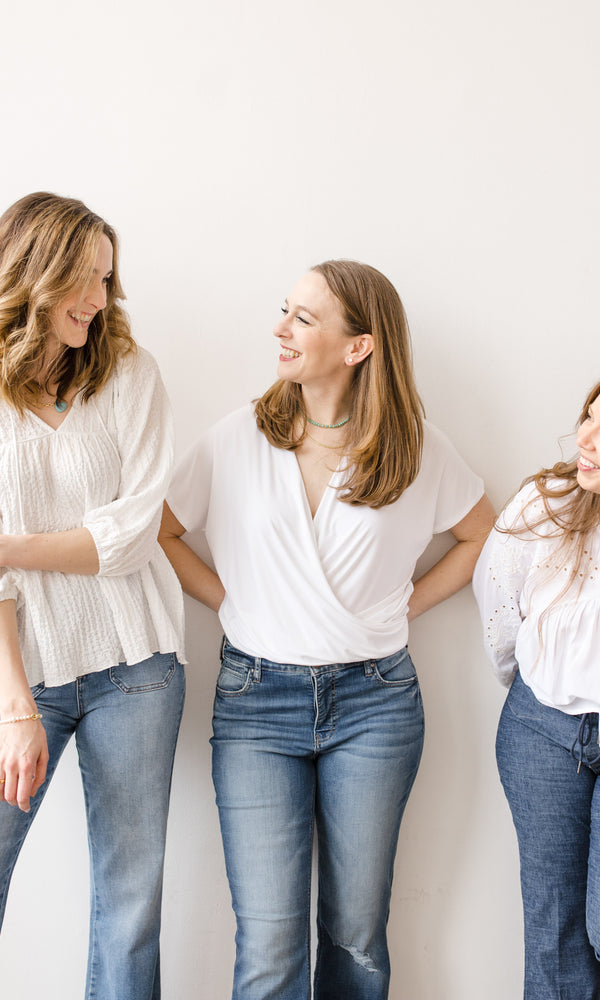 Three women on a white backdrop wearing white blouses and denim jeans from Vixen Collection in Seattle, WA | Women's Clothing Store and Gift Boutique 