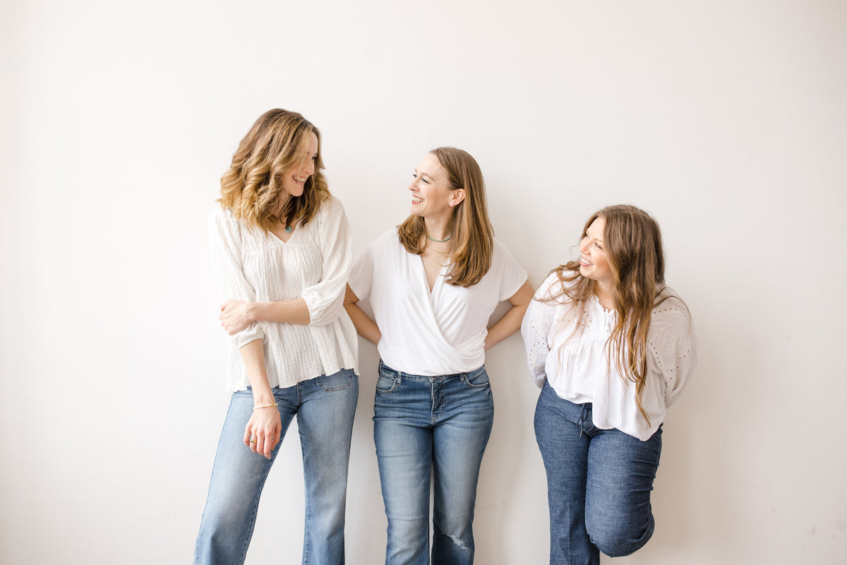 Three women on a white backdrop wearing white blouses and denim jeans from Vixen Collection in Seattle, WA | Women's Clothing Store and Gift Boutique 