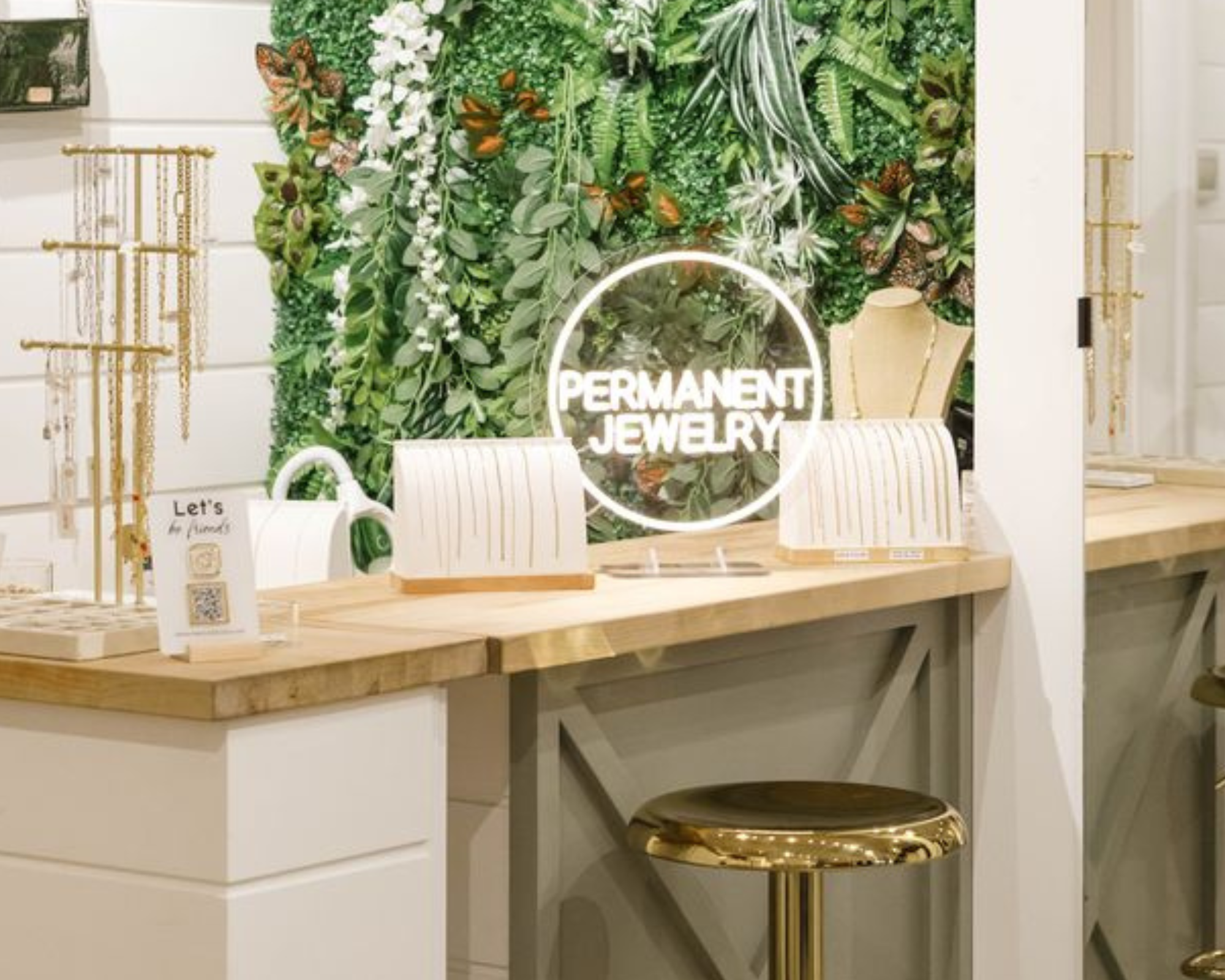 A decorative green living wall with the brand name 'VIXEN COLLECTION' at the top, set in a jewelry display area with a wooden counter, white cabinets, and a gold stool.