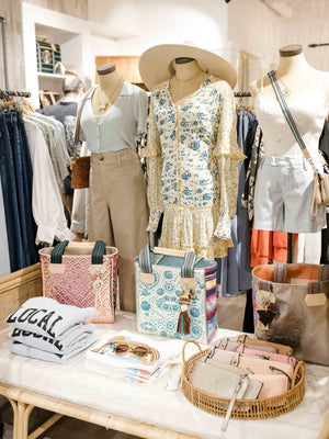 Display of clothing and accessories in a store with mannequins and products on a table.