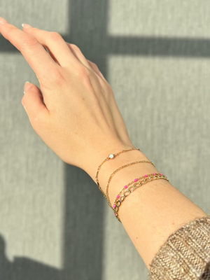 A woman's wrist wearing permanent jewelry over a grey shadowed back drop. Now available at Vixen Collection Boutique in Seattle, WA. 